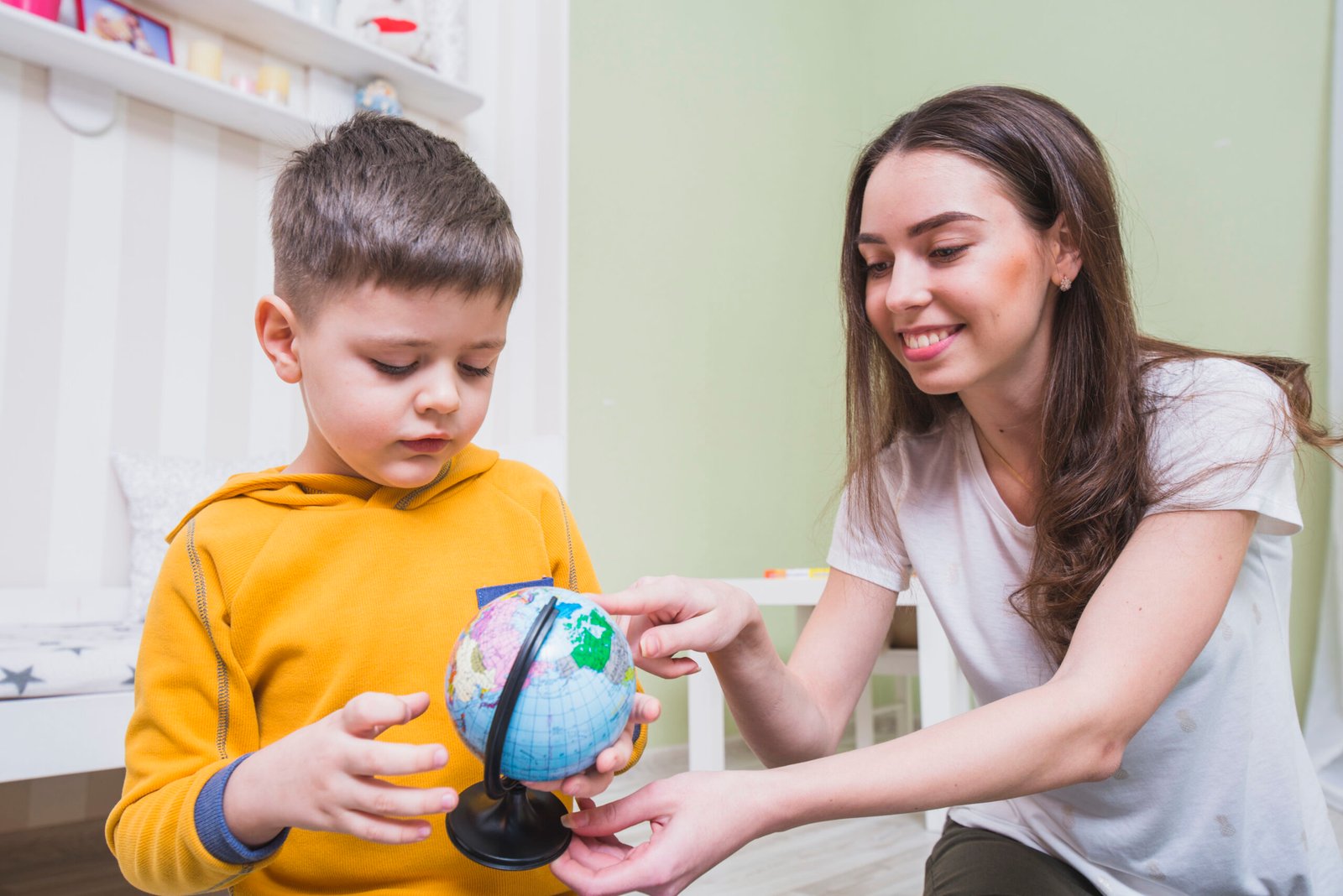 A woman guides a boy as he examines a globe, encouraging his interest in global cultures and geography.