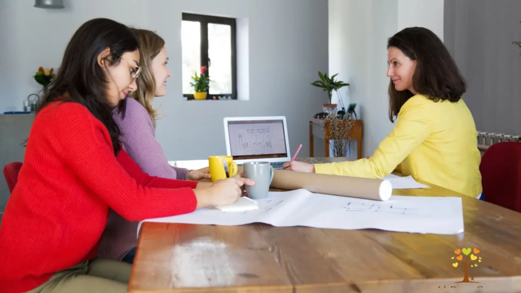 A table scene featuring three women seated together, focused on a laptop as they share ideas and work collaboratively.